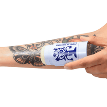 Load image into Gallery viewer, Applying a People of Substance full-size tattoo balm stick to a butterfly tattoo on a forearm
