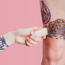 Load image into Gallery viewer, Pocket-size balm stick being applied to a tiger tattoo on a leg against a pink background
