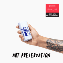 Load image into Gallery viewer, Hand holding the full-size balm stick, with a butterfly tattoo on the forearm and a NY NOW Best New Product Award finalist badge
